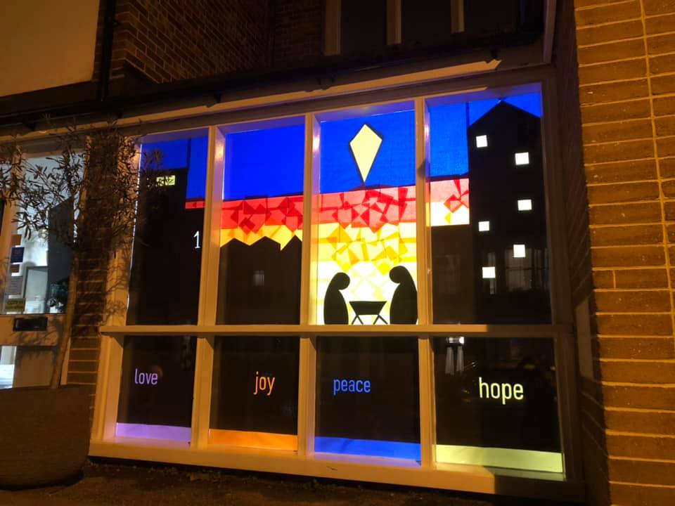 Window with words love, joy, peace and hope in the silhouette of London tower blocks and the simple nativity scene 